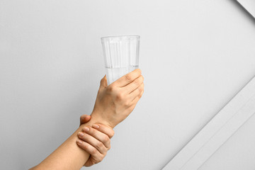 Woman suffering from Parkinson syndrome with glass of water against grey background