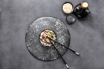 Boiled rice with vegetables in bowl and sauce on dark background