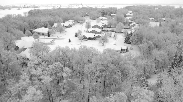 Very scenic small town neighborhood, trees covered with snow, homes blanketed in white, aerial drone view.