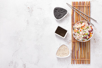 Boiled rice with vegetables in bowl, sesame and sauce on white background