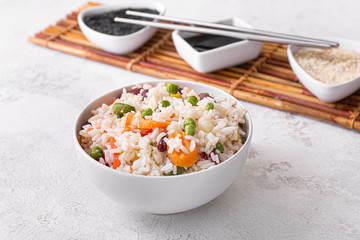 Boiled rice with vegetables in bowl on white background