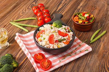 Boiled rice with vegetables in frying pan on wooden table