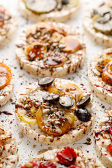 Rice wafers with a variety of fresh fruits, seeds, nuts and cream cheese sprinkled with chocolate sauce on a white background, top view. Rice cakes, the concept of a healthy breakfast or dessert
