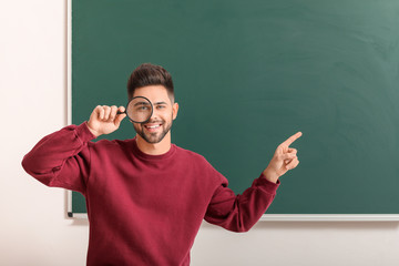 Male teacher with magnifier near blackboard in classroom
