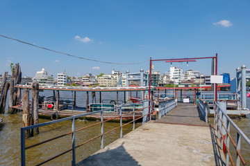 Outdoor sunny view of floating steel pontoon, pier or dock without people and small pontoon crossing river boat anchor beside pier, on Chao Phraya River, in Bangkok, Thailand.