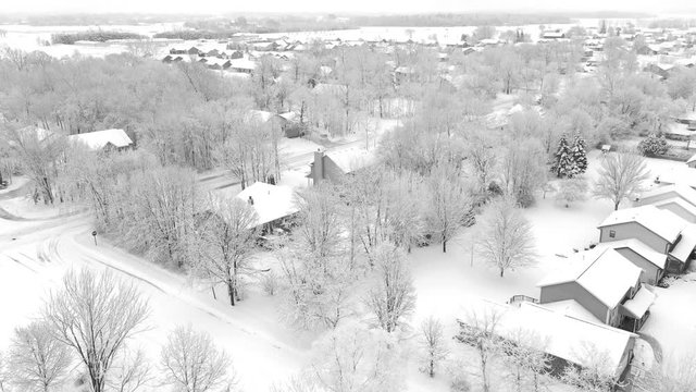 Very scenic small town neighborhood, trees covered with snow, homes blanketed in white, aerial drone view.