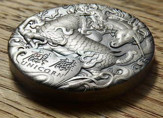 Macro of a dragon and unicorn on a silver coin, high relief. Chinese writing saying unicorn on a wooden background in sunlight