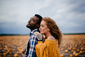 A young woman leaned against her husband's back while standing in a pumpkin field.