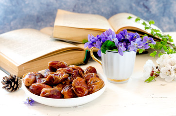 Bowl with sweet tasty dried date fruits in a composition with violet flowers and vintage books.