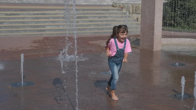 A kid plays in the fountain. Cheerful little girl is playing in the fountain.