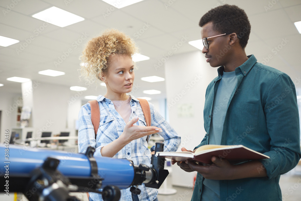 Wall mural waist up portrait of two students discussing astronomy project while standing by telescope in class 