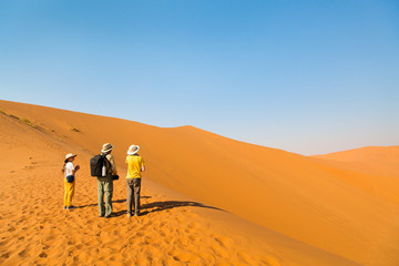 Fototapeta na wymiar Family climbing up red sand dune