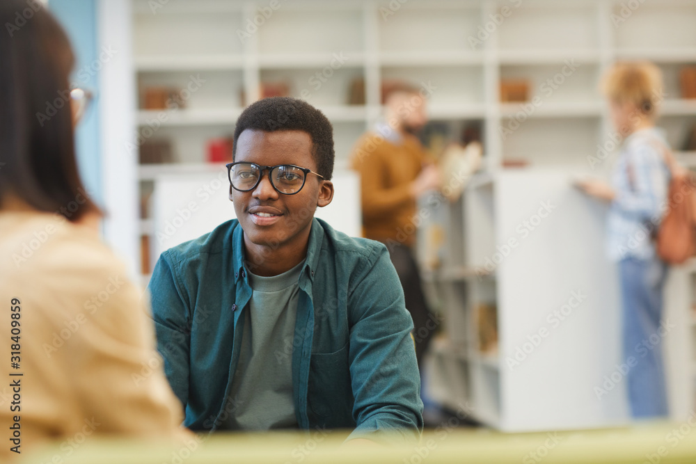 Wall mural portrait of smiling african-american student discussing project with partner while sitting at table 