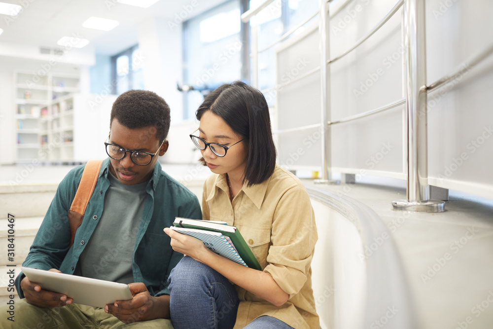 Wall mural portrait of two international students reading books together while working on project in modern col