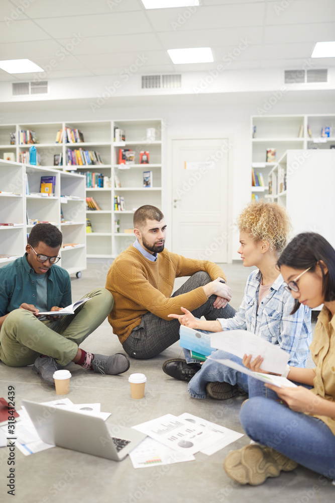 Wall mural full length view at multi-ethnic group of students sitting on floor in library and discussing projec