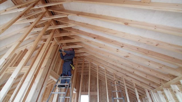 Interior of new frame house interior, and builder on high steel ladder nailing planks under ceiling