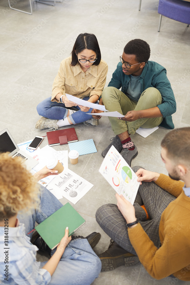 Wall mural high angle view at multi-ethnic group of students sitting on floor while working on project in colle