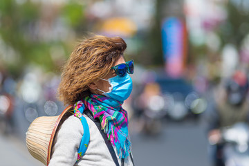 Woman wearing sanitary mask outdoors in Da Lat city centre Vietnam. Medical mask protection against risk of chinese flu virus epidemy in Asia. Anti smog mask traffic pollution.