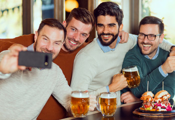 Group of happy friends make selfie with phone in beer pub