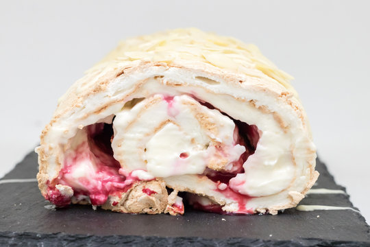 Meringue roll with white cream, red berries and nuts on a black tray on a white background