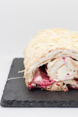 Meringue roll with white cream, red berries and nuts on a black tray on a white background