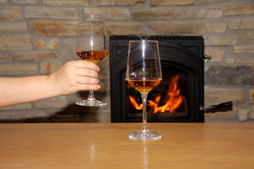 in front of a fireplace in which firewood burns with a bright flame, a man holds a glass of wine, a...