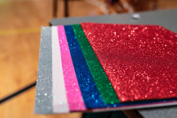 Upclose photo of a pile of colorful rectangular paper tiles covered with sparkling glitter laying in stack on a table