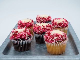 Rustic Metal Silver Tray Filled with Vanilla and Chocolate Cupcakes with White Frosting, Red, Pink and White Sprinkles, Decorated for Valentine’s Day against White Background.