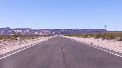 Old straight asphalt road with yellow dashed line leading into the horizon in the middle of nowhere, south Oregon.