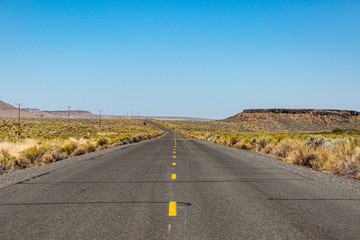 Old straight asphalt road with yellow dashed line leading into the horizon in the middle of nowhere, south Oregon.