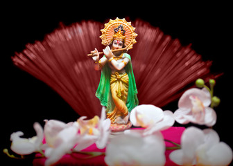 Statue of hindu god Krishna on black background with white orchid flowers. Text space. Selective focus.