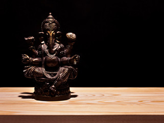 Hindu god Ganesha on black background. Statue on wooden table. Copy space.