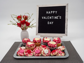 Happy Valentine’s Day Letter Board with Heart Flower Arrangement and a Rustic Tray Full of Decorated Cupcakes and Thumbprint Cookies covered in Frosting and Red, White and Pink Sprinkles.