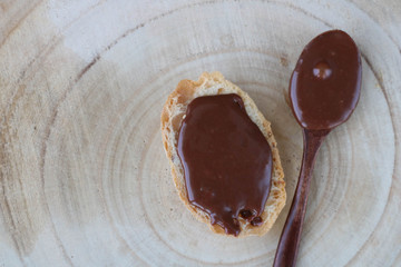 Wooden spoon with sweet chocolate cream and sandwich with chocolate spread on light wooden background. Top view