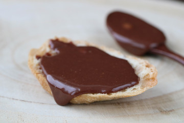 sandwich with homemade chocolate paste, wooden spoon with chocolate paste on light wooden table. Side view