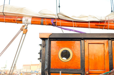Detail of a classic sailing tall ship, doghouse cabin with a round porthole, a sail flaked on a wooden boom and a sheet tackle.