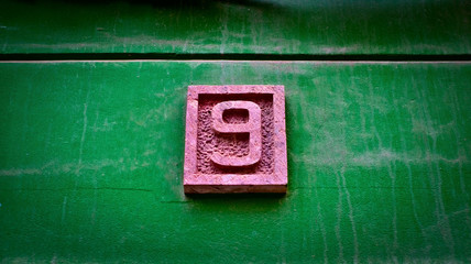 Number 9, nine, sandstone relief digit on a vivid green wall background.