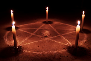 White pentagram symbol on concrete ground. Illuminated with candles. Dark background. Scary,...