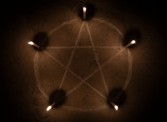 White pentagram symbol on concrete ground. Illuminated with candles. Dark background. Scary,...