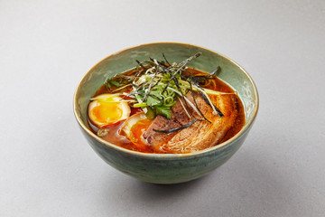 Ramen soup with meat and egg, red broth with herbs in a bowl 