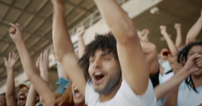 Young couple watching a sport event, jumping with hands raised, giving each other high five and hugging. Excited crowd of sports fans applauding and celebrating their team's victory. 
