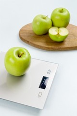 Close up photo of ripe green apple on gray digital kitchen scales. On the background several apples on wooden board. Healthy eating habits. Weighing products. Healthy food and diet concept.