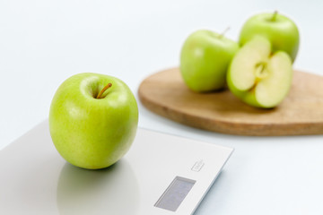 Close up photo of ripe green apple on gray digital kitchen scales. On the background several apples on wooden board. Healthy eating habits. Weighing products. Healthy food and diet concept.
