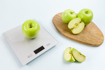 Ripe green apple on gray digital kitchen scales. On wooden board several whole apples and several sliced pieces. Healthy eating habits. Weighing products. Healthy food and diet concept.