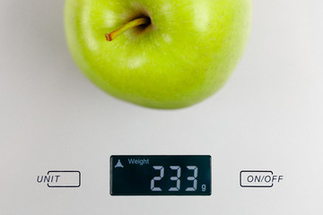 Cropped photo of green fresh apple on gray digital kitchen scales. Blue background. Flat lay, top view. Kitchen equipment concept. Raw vegan fruitarian and healthy food concept. Symbol of diet.