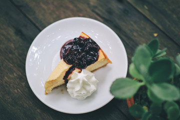 A delicious Piece of homemade cheesecake with black currant and blueberry sauce on white plate on wooden table.with fresh organic mint for dessert. Sweet summer pastry