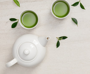 Cup of hot green tea with teapot, green tea leaves and dried herbs top view on the white stone table, Organic product from the nature for healthy with traditional style