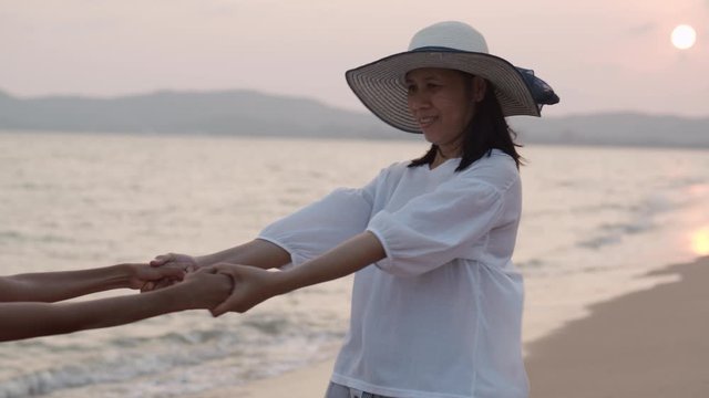 Happy asian family with mother and daughter holding hands to swing around on the beach at sunset in the summer of Thailand. Concept travel and tourist