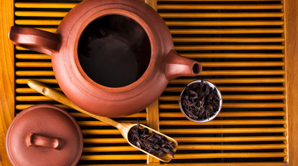Chinese tea ceremony. Ceramic tea pot, scoop and cup with the famous chinese oolong tea Da hong pao with vapour on a wooden background. Top view. - obrazy, fototapety, plakaty