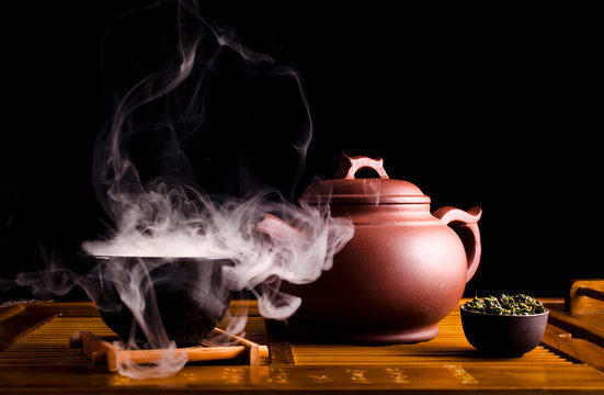 Chinese tea ceremony. Ceramic tea pot and cups with the famous chinese oolong tea Tieguanyin  with vapour on a black background.